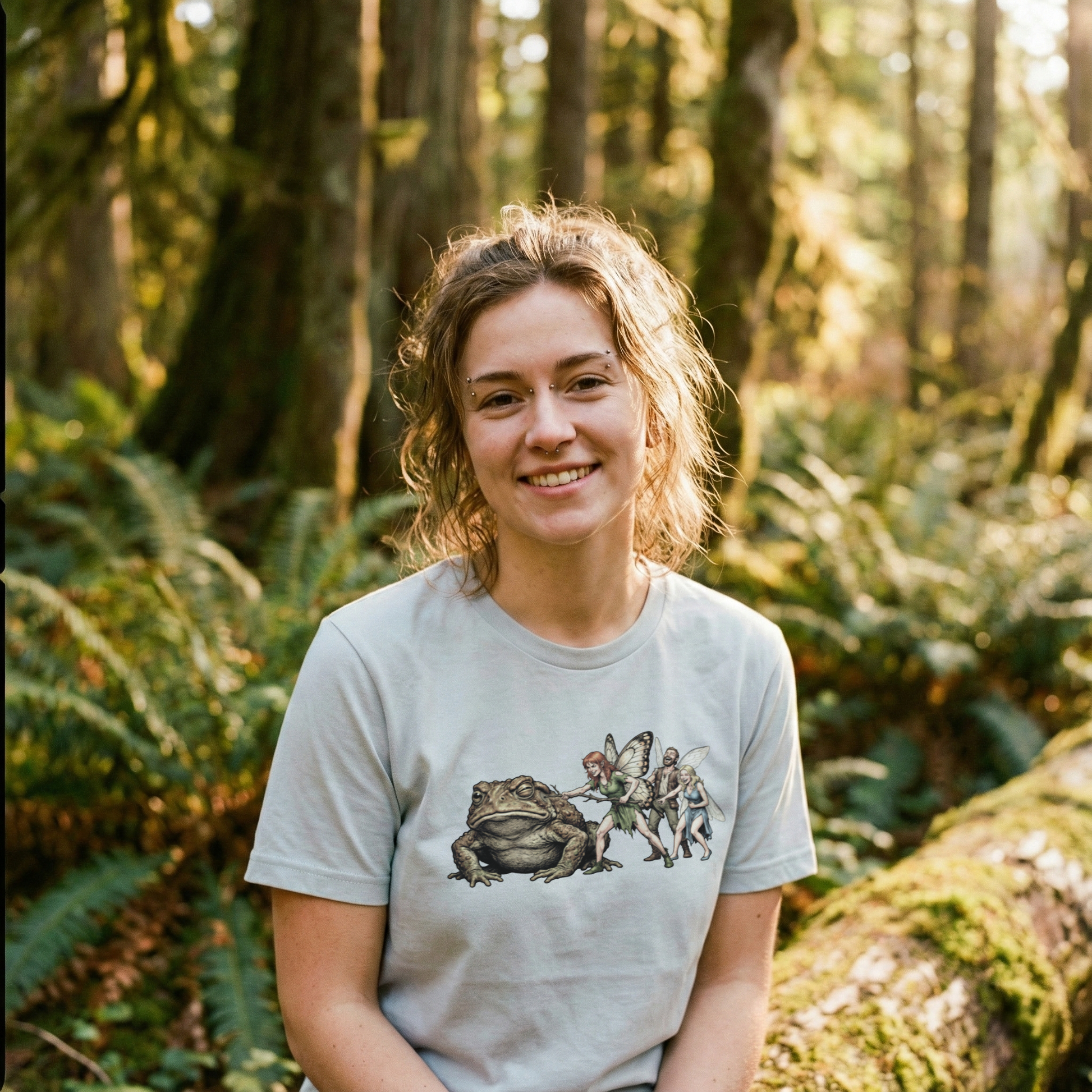 Graphic tee featuring a fairy poking a giant grumpy toad with a stick while other fairies laugh, organic cotton fantasy t-shirt.